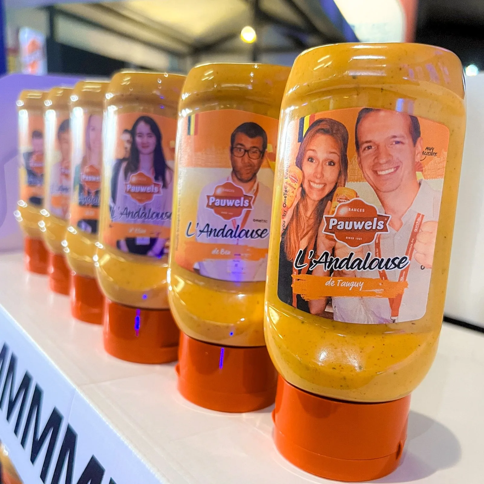 Pauwels Andalouse sauce bottles in a row, each with a different visitor's photo on the label
